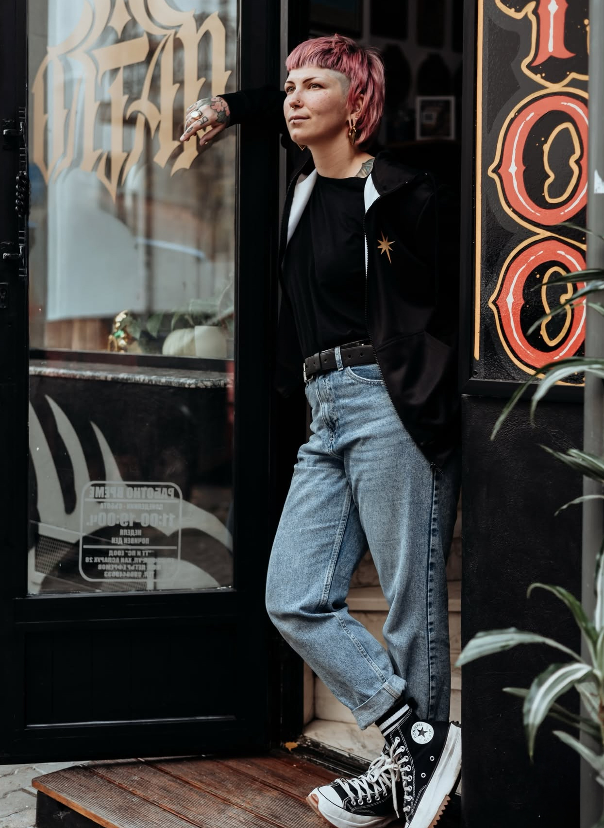 Katerina lehnt an Ladentür, lässiger Stil, Tattoos sichtbar.