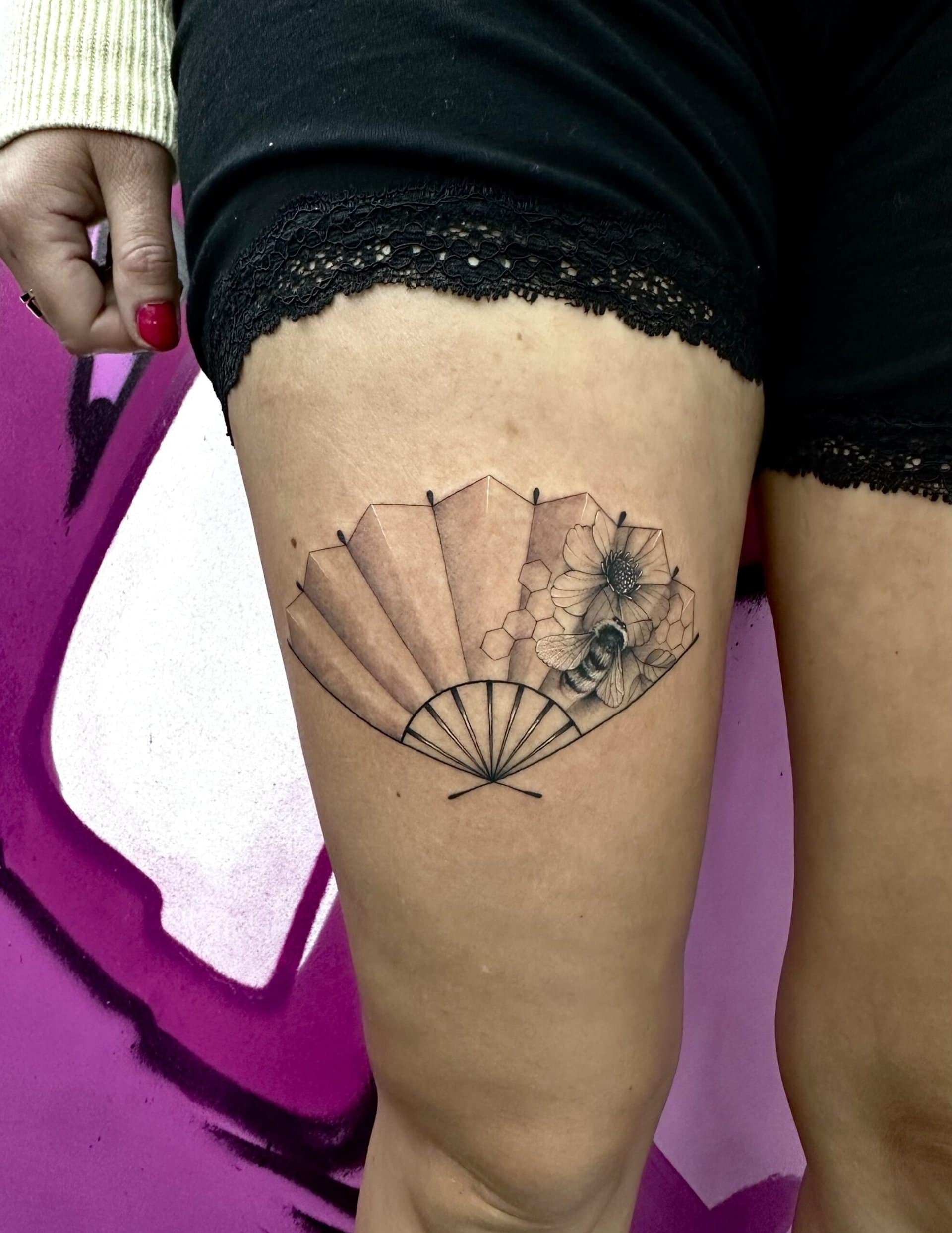 Handfächer Tattoo auf Oberschenkel vor pinkem Hintergrund.